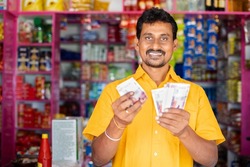 Happy smiling Groceries or Kirana Merchant small business owner Counting money by looking at camera - concept of Successful business, profit making, banking and finance.