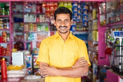 Portrait of successful Indian kirana or groceries businessman standing confidently with smile by looking at camera - concept of small business entrepreneur.