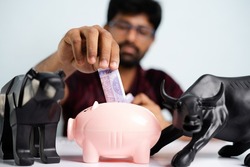 focus on money, Close up shot of Young man placing money inside the piggy bank - concpet of savings, investment in equity or mutual fund stocks.