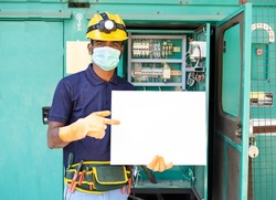Electrician with meidcal face mask and safety electrician with meidcal face mask and safety precautions holding empty sign board by looking at camera - concept of advertisement,promotion and job offer
