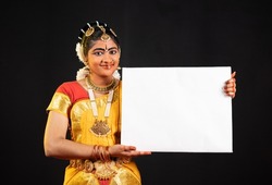 Indian beautiful bharatanatyam girl showing white empty board or placard by looking at camera - concept of announcement, advertisement and indian culture