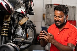 Young smiling mechanic using mobile phone in front of motors in showroom - concept of relaxation, taking break time and reading messages
