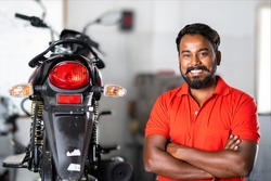 smiling motorbike mechanic standing with crossed arms by looking at camera - concept of repair or maintenance service and blue collar jobs