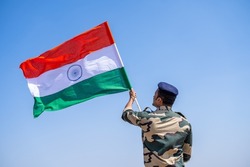 Indian army soldier holding waving Indian flag on top of mountain - concept of independence or repubilc day celebration, patriotisms and freedom