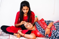 teenage daughter taking care of her by applying balm to forehead to sick mother while sleeping on daughters lap - concpet of caretaker, consoling, togetherness