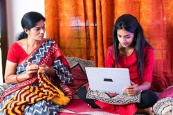 focus on daughter, mother busy stitching while daughter working on laptop - concept of conversation, parental care and togetherness