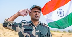 front view low angle shot of Proud Indian army soldier saluting while waving indian flag in background - concept of patriotic, nationalism, independence day celebration and honour
