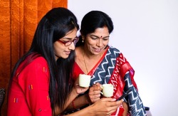 Mother and teenager daughter busy using mobile phone while having coffee - concept of parental caring, refreshment, leisure activities and relaxation.