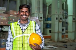 Portrait of happy smiling industrial worer with safety helmet in hand looking at with copy space - concept of safety measures, skilled labour and workforce.