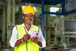Handheld shot of smiling Industrial worker with hardhat couting money - concept of earnings, banking or financial support and blue collar job