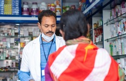 woman purchasing medicines at pharmacy store while pharmacist wearing mask below face - concept of healthcare, improper mask wear and covid-19 coronavirus protection.
