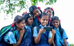 school girl kid playing video game on mobile phone while group of kids surrounded - concept of technology addiction, entertainment and togetherness.