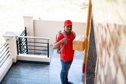 Delivery boy placing parcel in front of door after showing parcel to cctv or security camera - concept of security, safety and home courier service