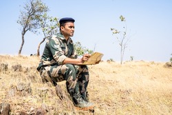 soldier seriously checking map while sitting on top mountain - concept of strategy planning, intelligence gathering and monitoring