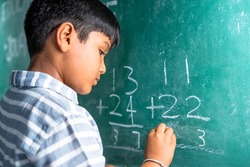 intelligent elementary school kid solving maths problem on chalkboard at classroom -concept of talented, brilliant student and education.