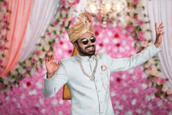Young man or Groom with Funky Eyeglasses dancing on wedding stage on decorated background - concept of Joyful Celebration, Excitement and marriage ceremony.