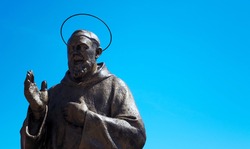 bronze statue of Padre Pio with blue sky in the background