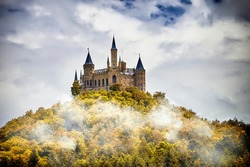 Castle on a wooded mountain in the fog under clouds, Hohenzollern, Germany