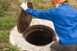 A working plumber opens a sewer hatch. Maintenance of septic tanks and water wells. selective focus