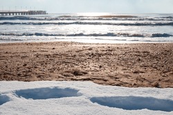 Cold sea with a pier and snow on the sandy shore. Black sea in winter.