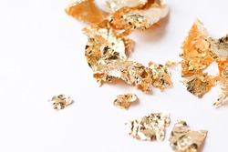Shiny pieces of gold sweat or gold leaf lying on white background