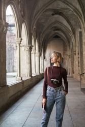 Pensive female traveler with vintage camera visiting ancient monastery church in European city