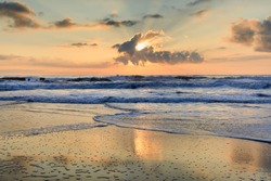Seascape of the Atlantic Ocean as the sun peeks from a cloud and glistens on the Cape Hatteras seashore in the Outer Banks, North Carolina.