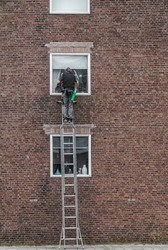 window cleaner standing high on a ladder to wash the windows of an apartment building