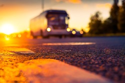 Sunset after rain, the headlights of the approaching bus on the highway. Close up view from the level of the dividing line, image in the orange-purple toning