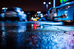 Rainy night in the parking shopping mall, the riding car. Close up view from the asphalt level, image in the blue tones