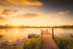 Sunset over the lake with a wooden bridge and boat. View from the shore, image in the yellow toning