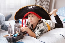 Little boy in pirate carnival costume plying at home with pirate ship toy. Cute kid boy having fun at halloween or birthday party.