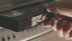 hand put Old VHS Video Cassettes iside the Old Video Recorder. Closeup. videotape cassette inside vcr , old technology concept 