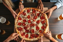 High angle shot of a group of unrecognizable people's hands each grabbing a slice of pizza