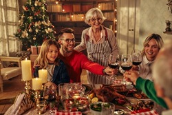 Family members sitting around dining table in the living room holding glasses and toasting, happy festive moment. They are celebrating Christmas together