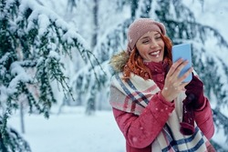 Woman typing on cellphone. Smiling girl in woolen winter hat and scarf typing on cellphone in cold winter day