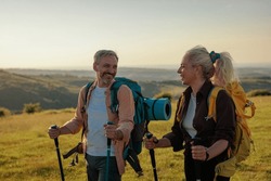 Middle age man and woman looking at each other while holding hiking pole. Senior couple exploring together on mountain. They are In casuals during weekend.