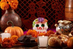 Traditional Mexican offering for the Day of the dead with a sugar skull, bread of the dead, Aztec marigold (Spanish: Cempasuchil), pumpkin, chocolate and candles. Typical cut paper on the background.