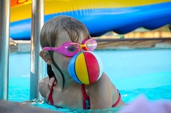young girl playing in swimming pool with a small ball in her mouth having fun.