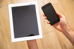 A tablet and a smartphone with blank screens with a copy space in male hands, top view. Using an electronic, mobile, portable devices at home.