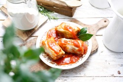 A composition of cabbage rolls in tomato sauce on a rustic plate, on cutting board, on light wooden boards. Meat-based, meat-stuffed delicatessen goods. Delicacy made of ground meat, rice and cabbage.