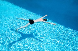 Man in black trousers swimming slowly in a swimming pool on a hot sunny day