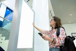 Woman with phone uses self-service desk with touch screen