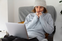 A woman in warm clothes with laptop. Low heating temperature in the house. Energy crisis concept