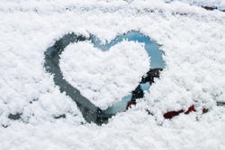 Heart shape drawn by hand on car window covered with fresh snow. Frozen rear windshield with heart on winter day