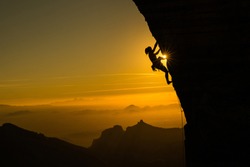 Silhouette of a female climber climbing a cliff during a beautiful orange sunset