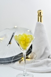 A festive glass with grapes on the background of a blurry clock and a bottle of champagne. Spanish tradition of eating twelve grapes to celebrate New Year.
