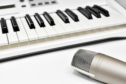 Professional studio microphone against blurred synthesizer keyboard background. Professional studio gear for voice and music recording.