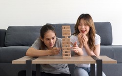 Two asian woman enjoy playing  wooden blocks game in the living room. Players take turns removing one block at a time from a tower constructed of 54 blocks.