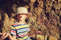 Funny boy in hat near gigant rock on beach